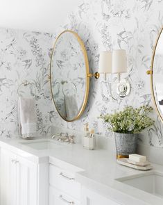 a bathroom with two round mirrors on the wall and white counter tops, along with flowers