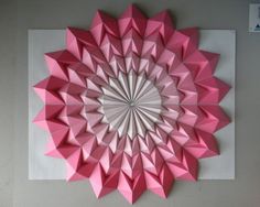 a pink origami flower is hanging on the wall in front of a white background