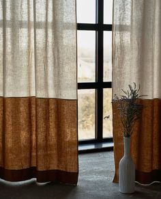 a vase with a plant in it sitting next to two curtains that have brown and white stripes on them