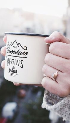 a person holding a coffee cup in their hand with the words adventure begins on it