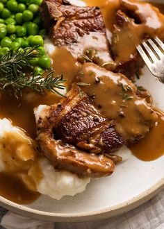 a white plate topped with meat and mashed potatoes covered in gravy next to peas