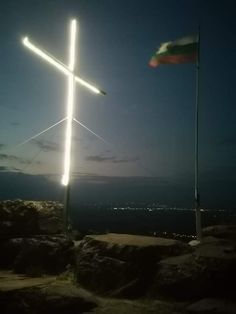 a cross on top of a hill with a flag flying in the background at night