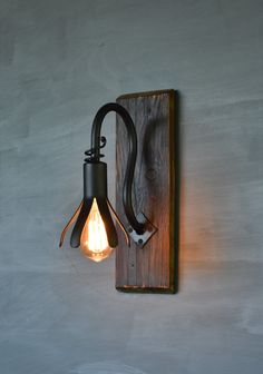 a light that is on the wall next to a wooden plaque with an iron hook