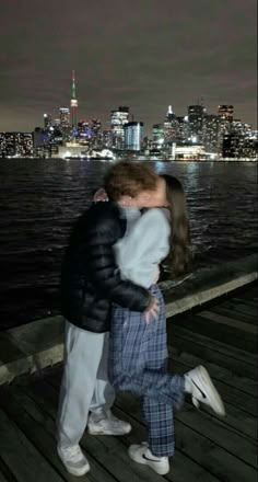 a man and woman kissing on a pier in front of a cityscape at night