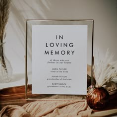 a sign that says in loving memory sitting on a table next to some dried flowers