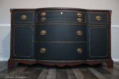 a black dresser with gold hardware on the top and bottom, sitting on a hard wood floor