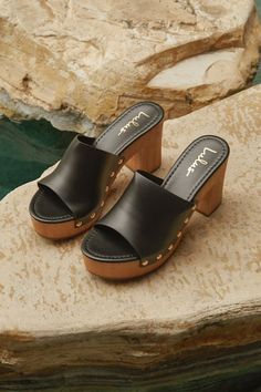 The Lulus Jaylani Black Platform Mule Sandals are the perfect combination of cute and cool for all your warm weather 'fits! Smooth faux leather shapes these essential sandals that have an almond footbed and a wide vamp strap with shiny gold stud accents along the side, all atop a 1.25"" toe platform. Easy slide-on design makes for effortless, everyday styling, while a sturdy wood-look block heel completes the classic clog-inspired look! 3. 75" wood-look block heel. Lightly cushioned insole. Rubb Chic Synthetic Clogs With Open Heel, Chic Synthetic Clogs With Stacked Heel, Chic Open Toe Clogs With Cushioned Footbed, Summer Synthetic Clogs With Stacked Heel, Chic Clogs With Cushioned Footbed And Block Heel, Chic Sandals With Wooden Heel, Beach Clogs With Block Heel In Synthetic, Chic High Heel Clogs For Beach, Chic Beach Clogs With Heel Strap