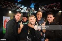 four men posing for the camera in front of a stage with one man giving the peace sign