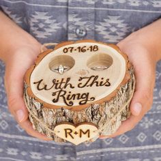 a person holding a wooden ring holder with two rings on it's face and the words, with this ring