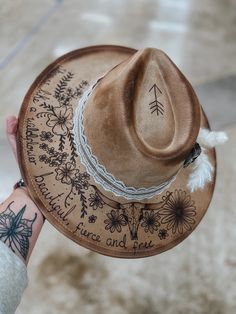 This is a tan suede hat with flowers, words, and a longhorn skull burned in.  Comes with everything you see on the hat as well.  This hat is adjustable and fits MOST head sizes.  Keep in mind each hat is free hand burned so can differ slightly. Lainey Wilson Hats, Western Hats For Women, Hat Burning, Custom Cowboy Hats, Lainey Wilson, Suede Hat, Painted Hats, Hand Burn, Boho Hat