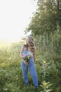 a woman standing in tall grass holding flowers