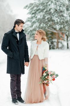 a man and woman standing in the snow holding hands