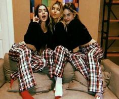 three women sitting on top of a couch wearing matching plaid pajama's