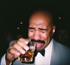 a man in a tuxedo drinking from a glass with a moustache on his face