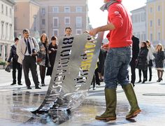 a man holding a skateboard in the middle of a city square with people standing around