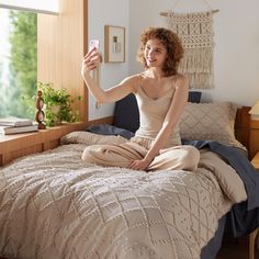 a woman sitting on a bed taking a selfie with her cell phone in the bedroom