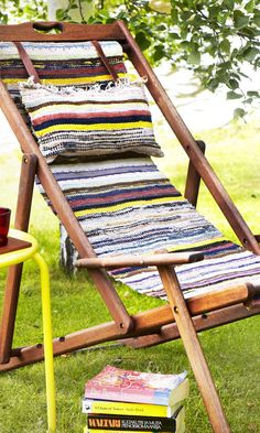 a wooden lawn chair sitting on top of a lush green field next to a pile of books