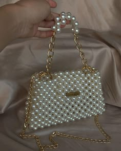 a hand holding a white purse with pearls on it