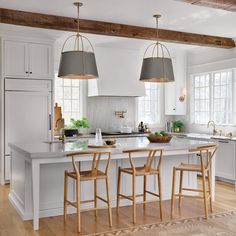 a kitchen island with three stools in front of it and two lights hanging from the ceiling