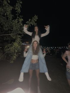 two young women standing next to each other with their arms in the air and one woman sitting on top of her