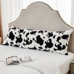 a cow print pillow sitting on top of a bed next to a cup and magazine