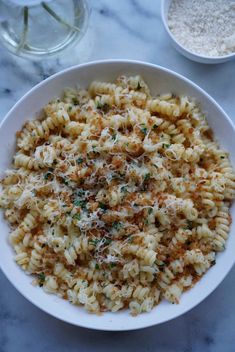 a white bowl filled with macaroni and cheese on top of a marble table