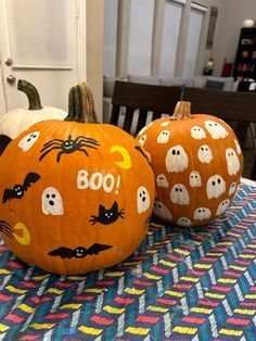 two pumpkins sitting on top of a table covered in ghost and bat designs, with the words boo written on them