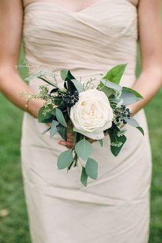 a woman in a dress holding a white rose and greenery bouquet on her wedding day