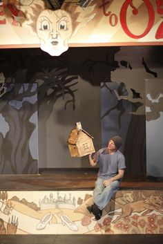 a man sitting on top of a wooden bench in front of a wall with paintings