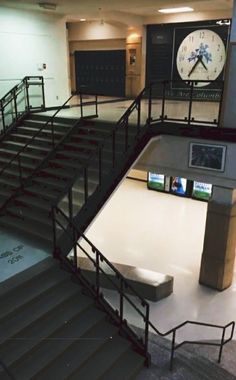 an empty lobby with stairs and a large clock on the wall above it's railings