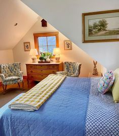 a bed sitting under a window in a bedroom next to two chairs and a dresser