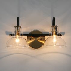 two lights that are on the side of a wall mounted light with clear glass shades