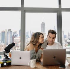 a man and woman sitting at a table with an apple laptop