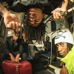 two men sitting on a bus with their hands in the air and one holding a red suitcase