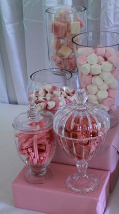 pink and white candies in glass containers on top of a pink cake stand with other sweets