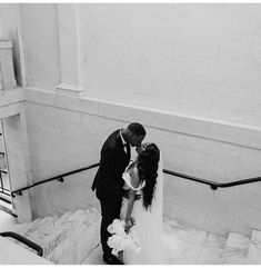 a bride and groom kissing on the stairs at their wedding reception in black and white