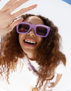 a woman wearing purple sunglasses and holding her hand up to the camera