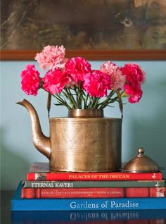 pink carnations are in a brass teapot on top of books and a painting