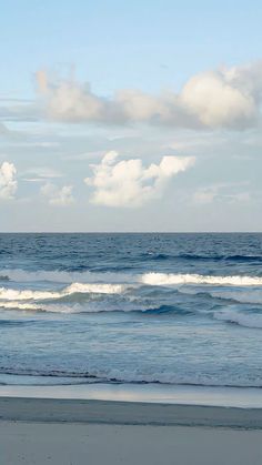 a person walking on the beach with a surfboard in hand and clouds in the background