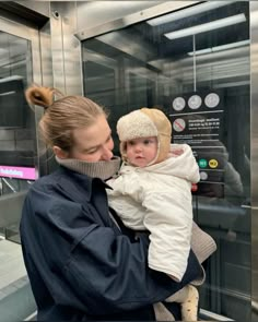 a woman holding a baby in her arms while standing next to a glass elevator door