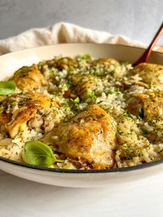 a white bowl filled with chicken and rice covered in sauce, garnished with green leaves