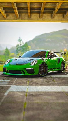 a green sports car is parked under an overpass with mountains in the back ground