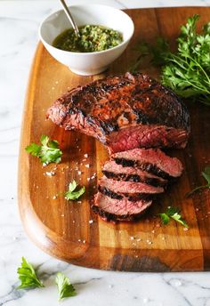 a steak on a cutting board with parsley next to it and a bowl of sauce