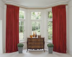 two vases are sitting on a dresser in front of a window with red drapes