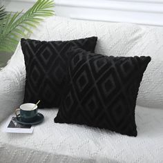 two black pillows sitting on top of a white couch next to a cup and saucer