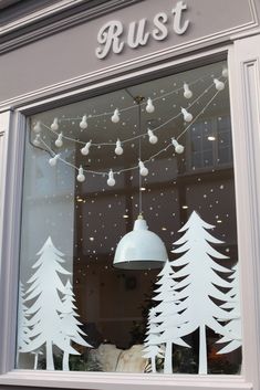 a store window with white christmas trees and lights hanging from it's windowsill