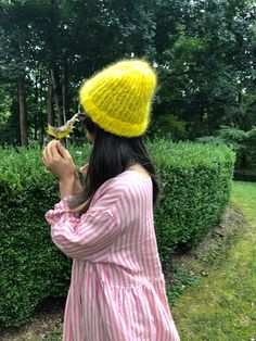 a woman wearing a yellow knitted hat and holding a small bird in her hand