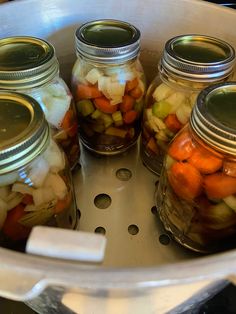 four jars filled with pickled vegetables sitting on top of a stove