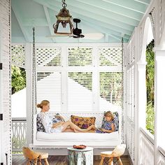 two women sitting on a porch swing bed with white shutters and wood flooring