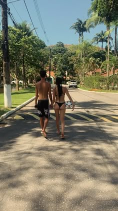 two people are walking down the street in swimsuits and one is holding a surfboard